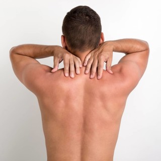 Rear view shirtless man having back pain standing against white wall