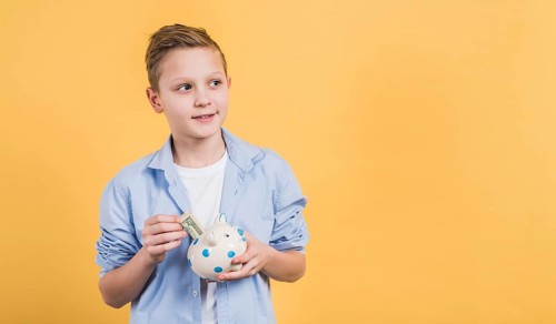 Smiling boy inserting currency note ceramic white piggybank