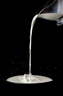 Pitcher with milk pouring on a plate with splash effect on a black background