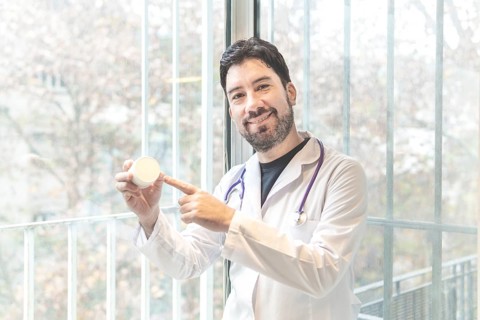 Handsome hispanic man wearing doctor uniform and stethoscope at medical clinic amazed and smiling to the camera while presenting with hand and pointing with finger