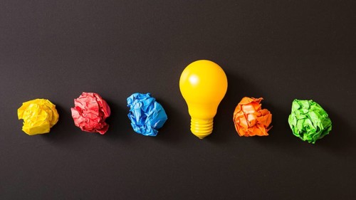 Colorful crumpled paper ball with yellow light bulb against black background