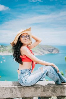 Beautiful tourist girl in a viewpoint with a beach in the background. Happy tourist sitting at a viewpoint looking at the camera with bay in the background