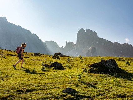 Woman hiking across alpine meadow in front of the peaks of the Bischofsmuetze
