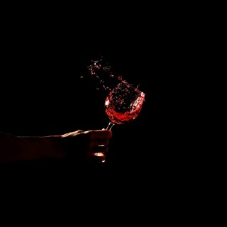 Person s hand holding glass red wine splashing out glass
