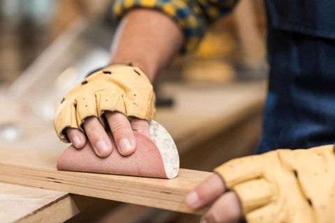 Close up male carpenter rubbing down wood with sandpaper