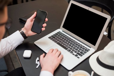 Young businessman using laptop looking smartphone screen