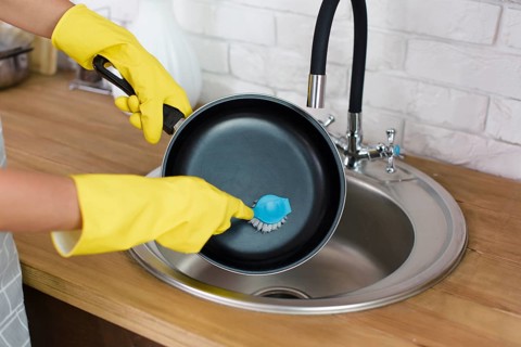 Person hand with yellow glove washing pan with brush kitchen