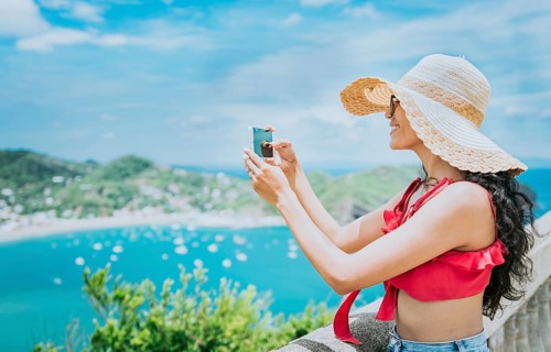 Traveler girl photographing a bay from a viewpoint. Happy tourist woman in a hat photographing a viewpoint