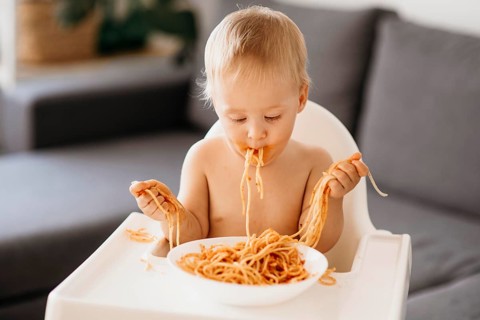 Front view baby boy playing with pasta his highchair