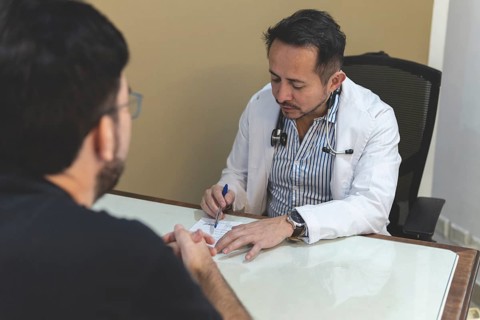 Latin doctor sitting at his desk writing a prescription to his patient