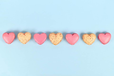 Pink and yellow heart shaped French macaron sweets in a row on blue background