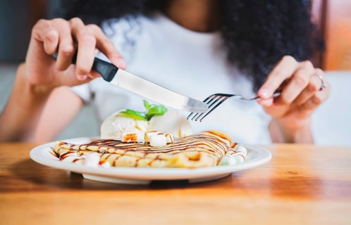 Woman hands eating chocolate crepe and ice cream with fork. Close up of woman eating a chocolate crepe with fork