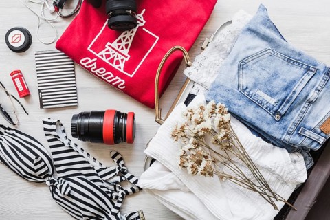 Overhead view travelling bag with female outfits flowers