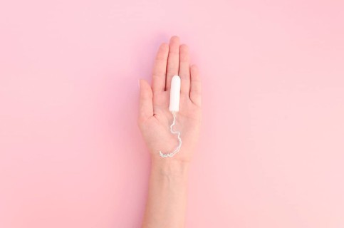 Hand holding tampon pink background