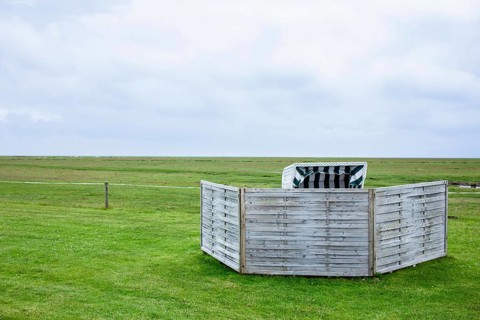 Beach chair in a meadow on the Wadden Sea with windbreak in front of it