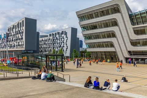 Students in front of modern buildings on the campus of the University of Economics WU