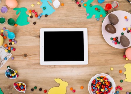 Blank digital tablet surrounded with colorful gems candies easter eggs paper cutout bunny wooden table