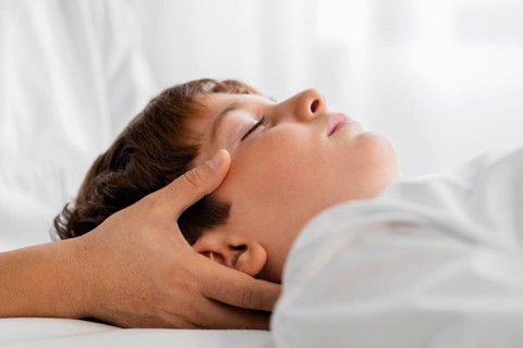 Female osteopathist treating child by massaging his head
