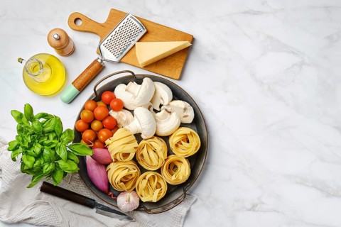 Top view of raw ingredients for mushroom pasta on marble background
