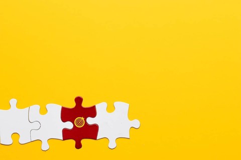 Red jigsaw puzzle piece with dartboard symbol arranged with white piece yellow background