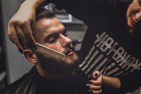 Hairdresser combing beard stylish man