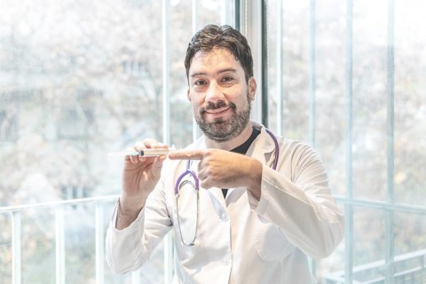 Handsome hispanic man wearing doctor uniform and stethoscope at medical clinic smiling to the camera while presenting a vaccine