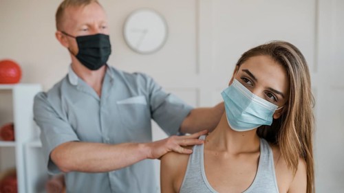 Male physiotherapist wearing medical mask during therapy session female patient