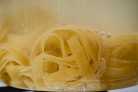 Closeup view of fettuccine pasta into boiling water in a transparent glass saucepan