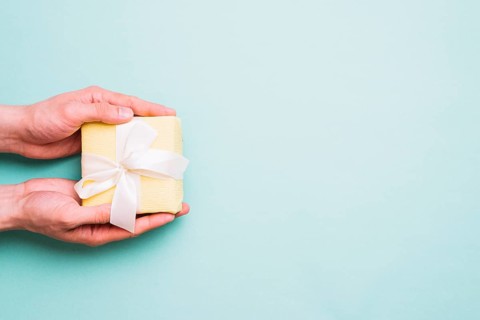 Person s hand holding small gift box against blue background