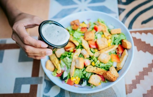 Concept of healthy food and lifestyle. Hand putting dressing on a caesar salad