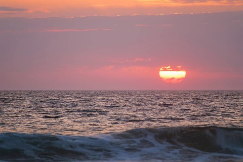 Ocean waves on sunset with setting sun background