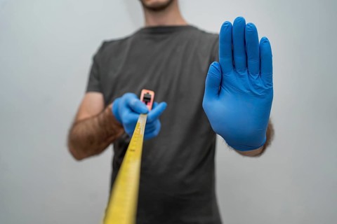 Man with gloves holding tape measurer social distancing