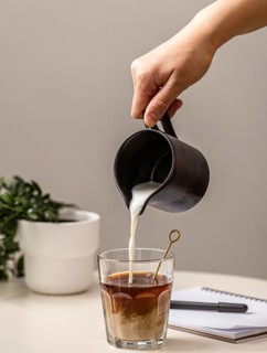 Person pouring cream coffee glass