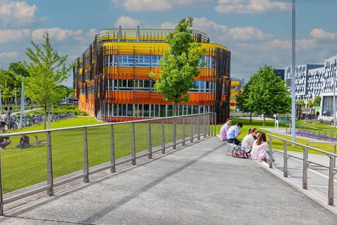 Students sitting in front of modern buildings on the campus of the University of Economics WU