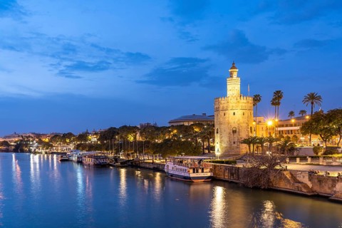 On the banks of the Guadalquivir River with the historic Torre del Oro tower at dusk