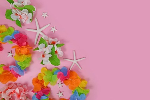 Bright flower lei necklaces on side of pink background with copy space