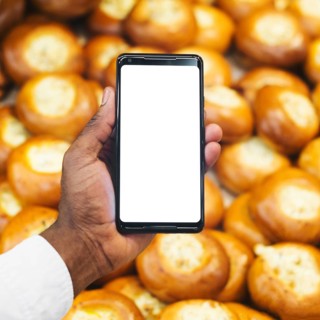 Crop hand with smartphone pastry background