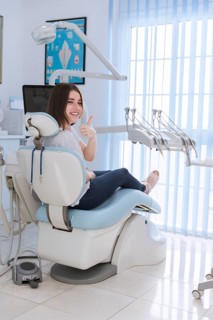 Smiling female patient sitting chair showing thumb up dental clinic