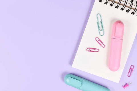Clipboard with pink and blue text markers and paper clips on purple background with empty copy space