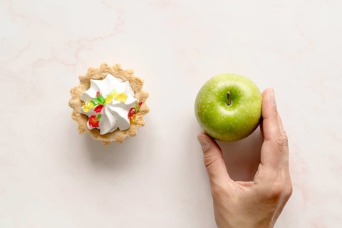 Human hand holding green apple near tart cake backdrop