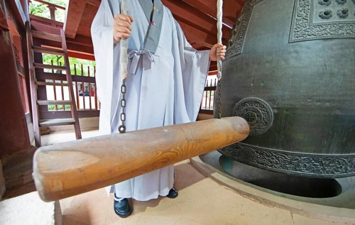 Korean monk strikes the bell with a wooden trunk