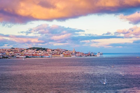 View of Lisbon over Tagus river from Almada with yachts tourist boats and moored cruise liner on sunset with dramatic sky. Lisbon