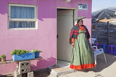 Herero woman in traditional colourful dress in front of her house in township near Swakopmund