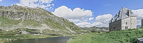 Photo with reduced dynamics saturation HDR of view on left mountain lake right historical hotel accommodation Ospizio San Gottardo Sankt Gotthard Hospice with historical building fabric from year 1237...