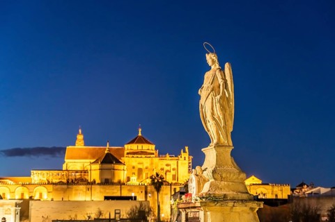 Statue of the Archangel Raphael on the Roman Bridge and the Mezquita at dusk