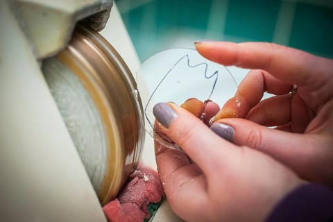 A woman grinds a lens at an optician's shop