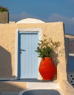 Red vase in front of yellow wall with blue door