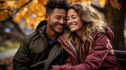 Happy warmly dressed young loving multi-ethnic couple laughing as they enjoy the beautiful fall leaves in the park