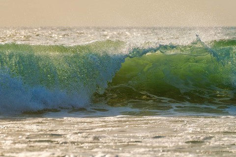 Breaking ocean wave on sunset backlit with sun. Fonte da Telha