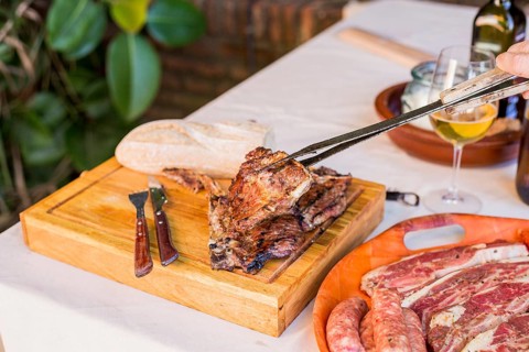 Person holding fresh grilled beef steak with tong wooden board